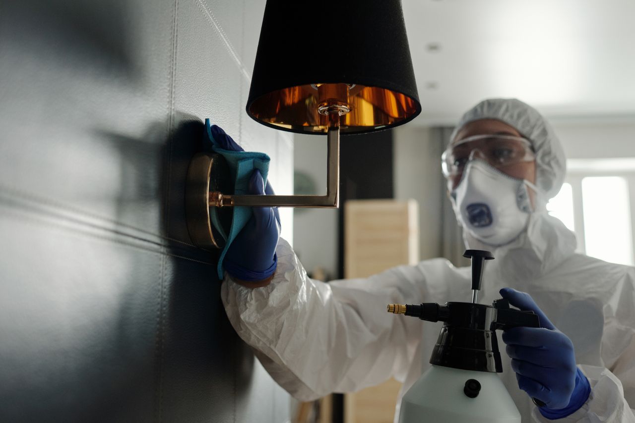 gallery-02 A person wearing protective gear sanitizes a wall lamp to prevent virus spread.