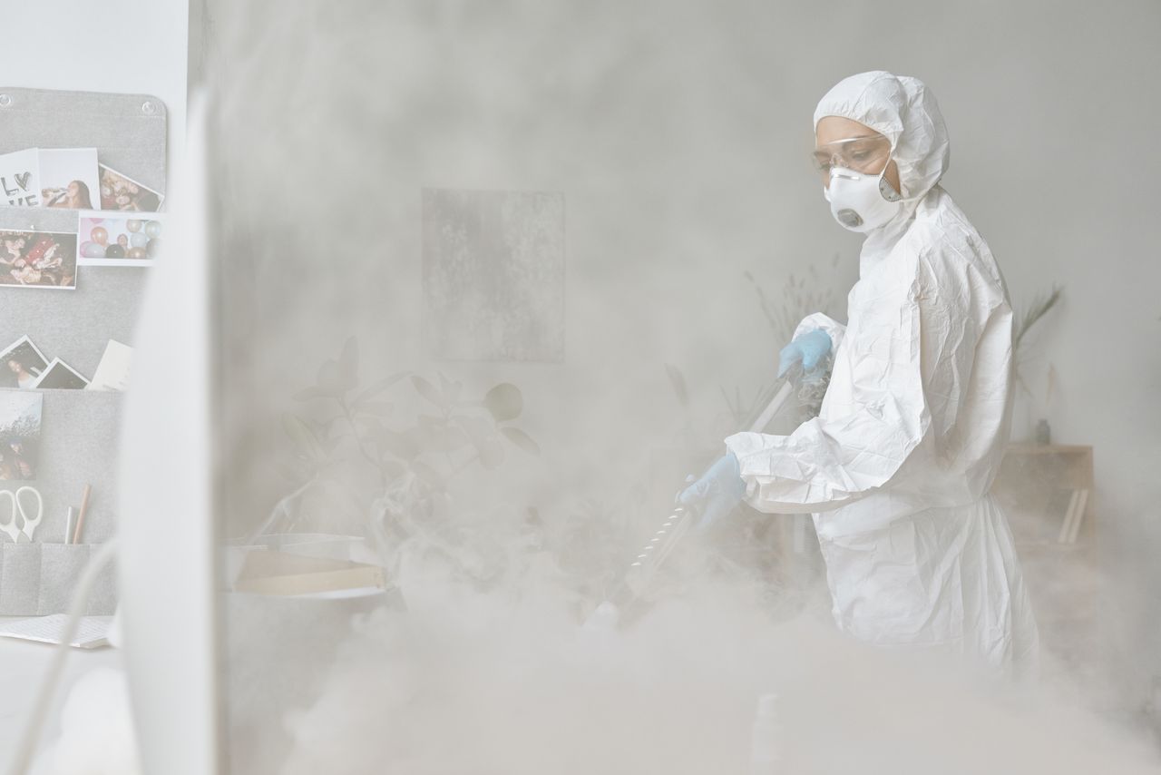 gallery-05 A woman in a protective suit disinfects an indoor space with fogging equipment.